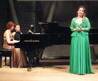 Ferzan in a long green gown on stage beside a grand piano