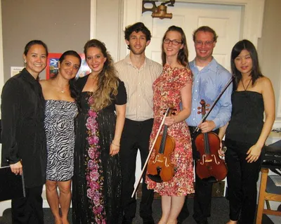 A group of seven musicians posing together, two of them holding violins