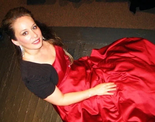 Ferzan in a black top and a flowing red satin skirt, reclining on a stage